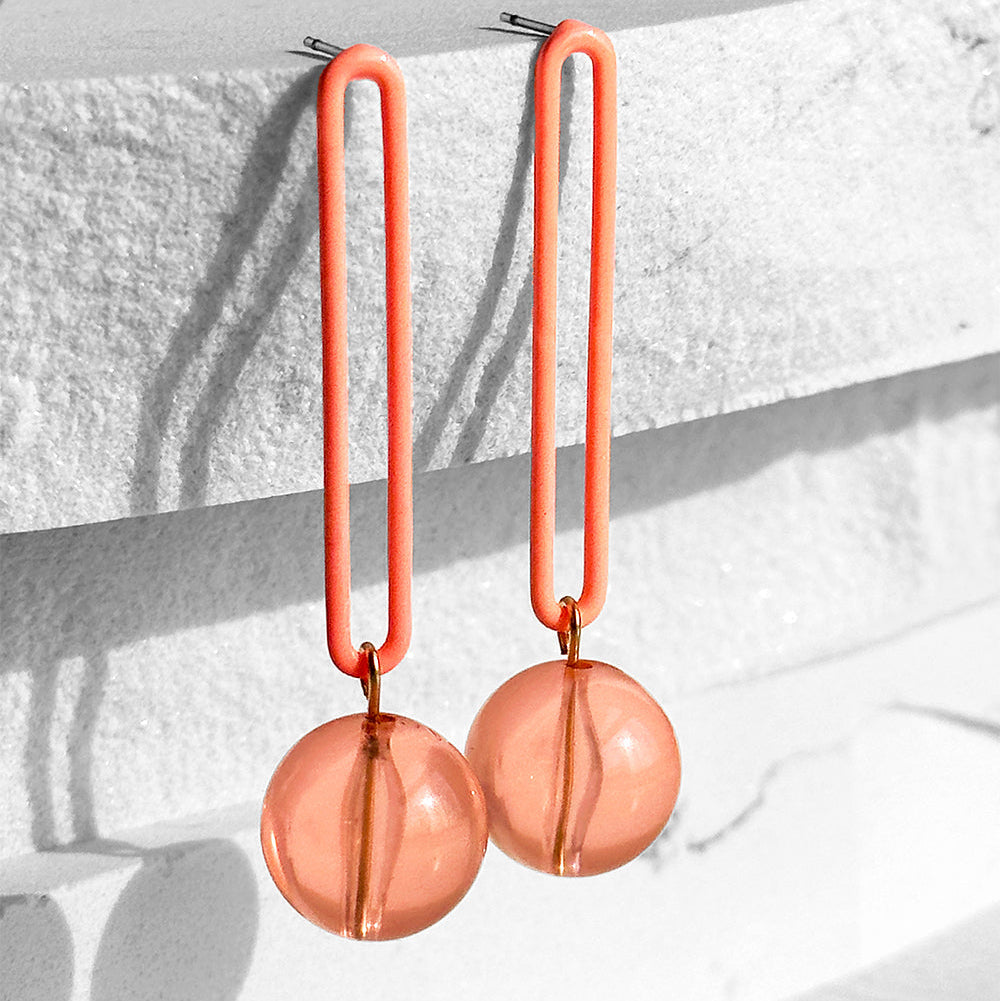 Coral-colored earrings with spherical drops on a textured white surface.