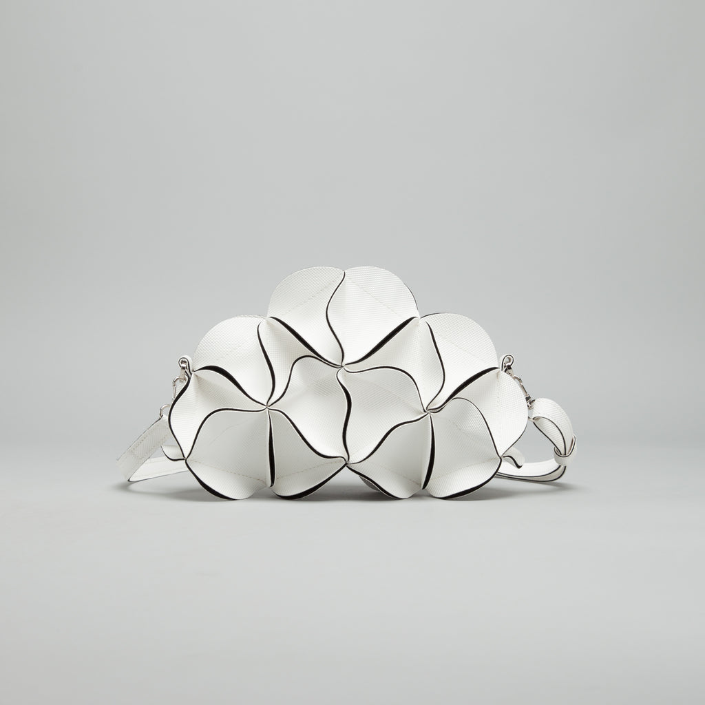 A white segmented, flower-like shoulder bag with black piping details and a silver-toned strap, displayed on a neutral gray background.