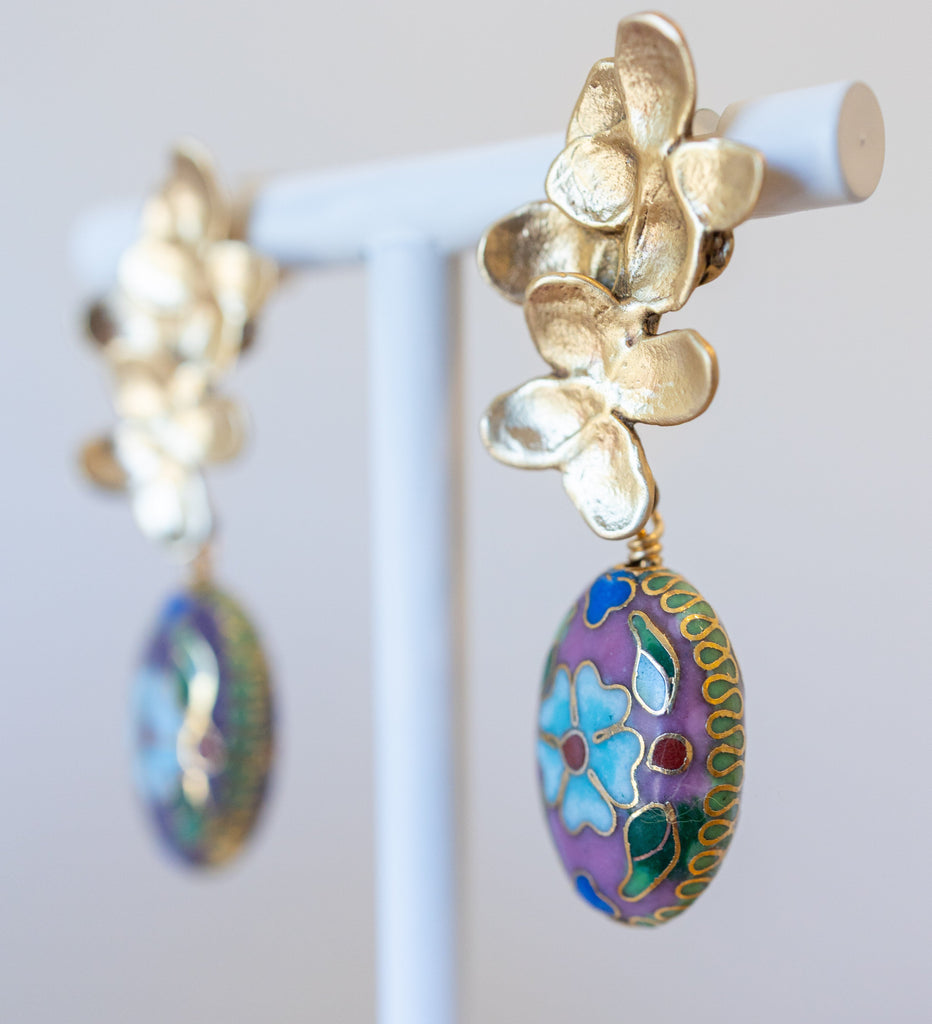 Gold earrings with colorful floral designs on a white stand