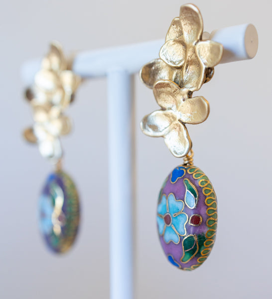 Gold earrings with colorful floral designs on a white stand