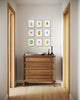 Wooden dresser with decorative items and gallery wall of botanical spring art in a hallway