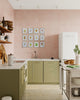 Modern kitchen with green cabinets, white appliances, and a pink wall with botanical artwork gallery wall.