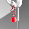 Red earring hanging from a white ear model against a gray background