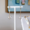 Gold earrings with clear spherical beads on a white stand against a blurred background