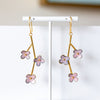 Gold earrings with pink floral designs on a white stand against a neutral background