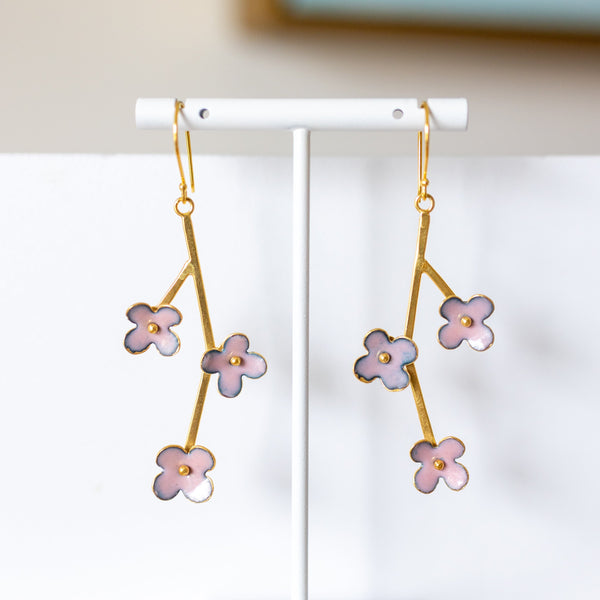 Gold earrings with pink floral designs on a white stand against a neutral background