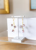 Floral earrings on a white stand against a neutral background
