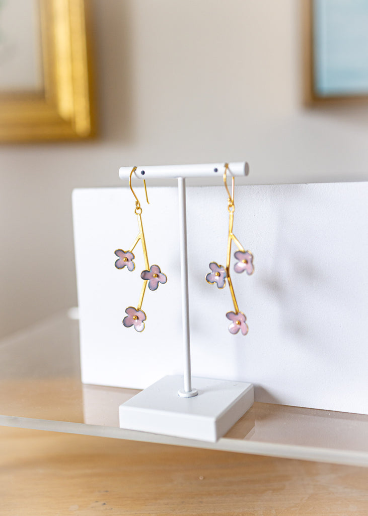 Floral earrings on a white stand against a neutral background