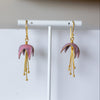 Pink earrings with gold hooks on a white stand against a light background