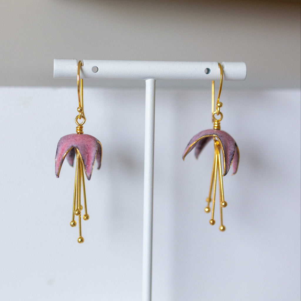 Pink earrings with gold hooks on a white stand against a light background