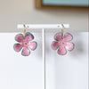 Pink flower-shaped earrings on a white stand with a neutral background