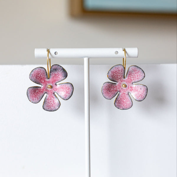 Pink flower-shaped earrings on a white stand with a neutral background