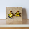 Pair of yellow flower-shaped earrings on a brown card with 'Jewelry Addict' branding.