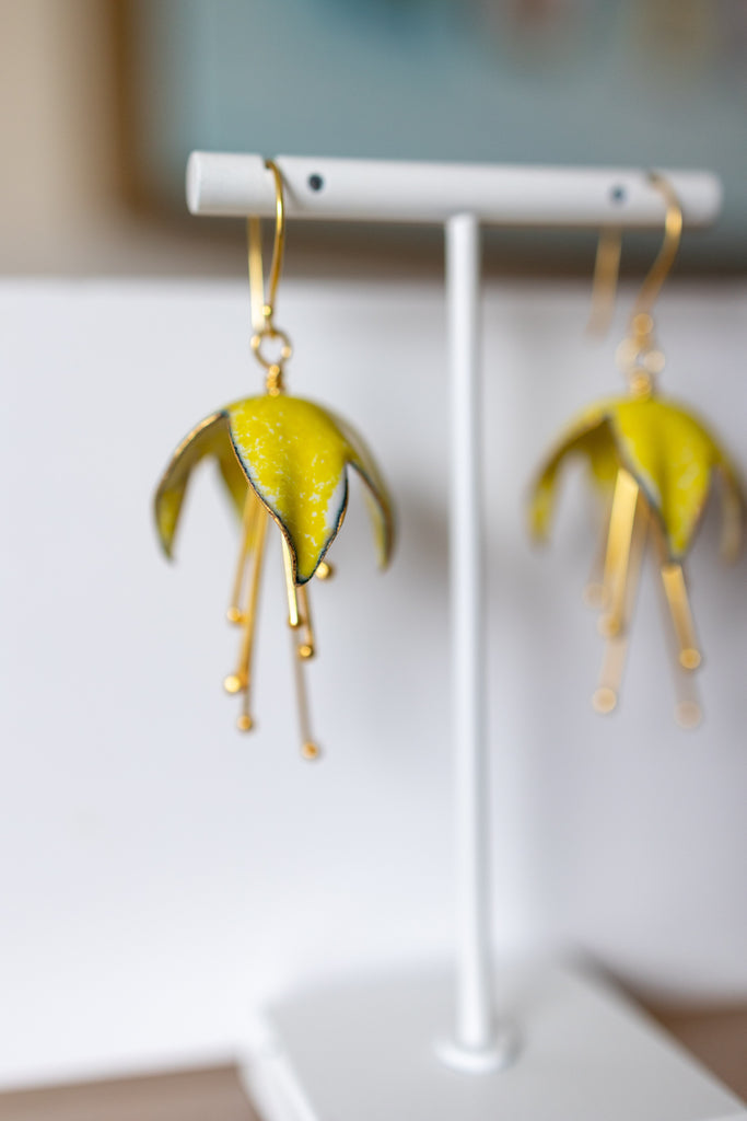Pair of yellow and gold earrings on a white stand.