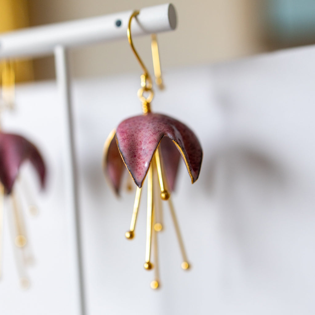 Purple and gold earrings on a white stand with a blurred background