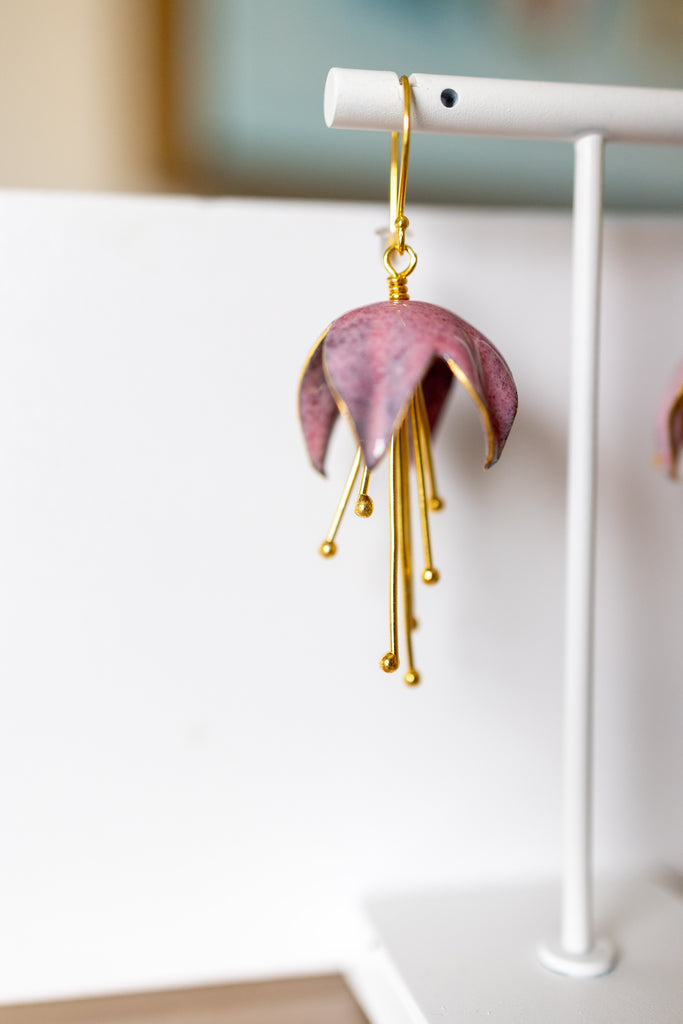 Pink flower-shaped earring with gold accents on a white stand.