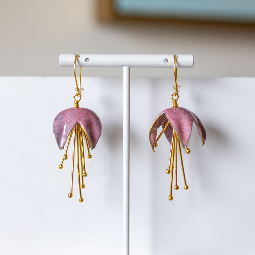 Pink earrings with gold accents on a white stand against a neutral background