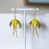 Yellow floral earrings on a white stand against a neutral background