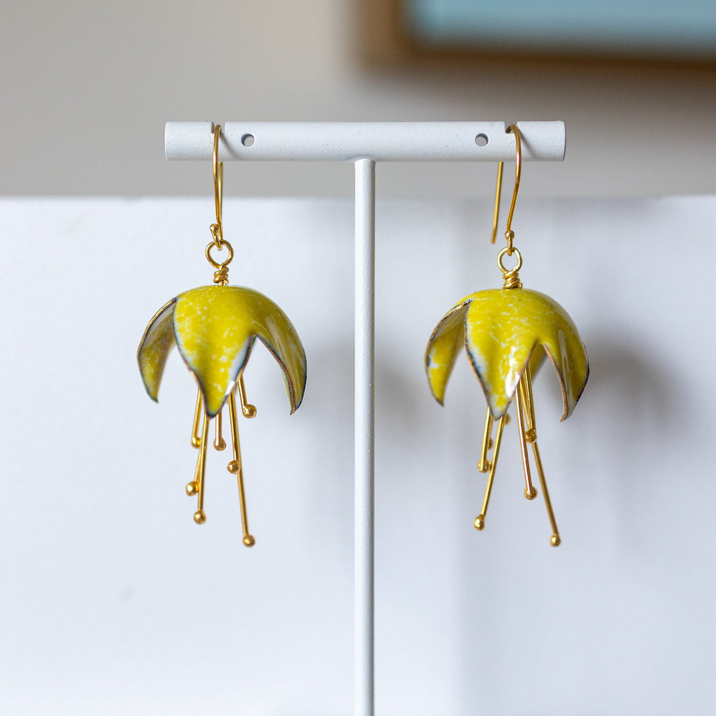 Yellow floral earrings on a white stand against a neutral background