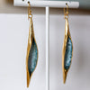 Gold and blue earrings on a white stand with a blurred background