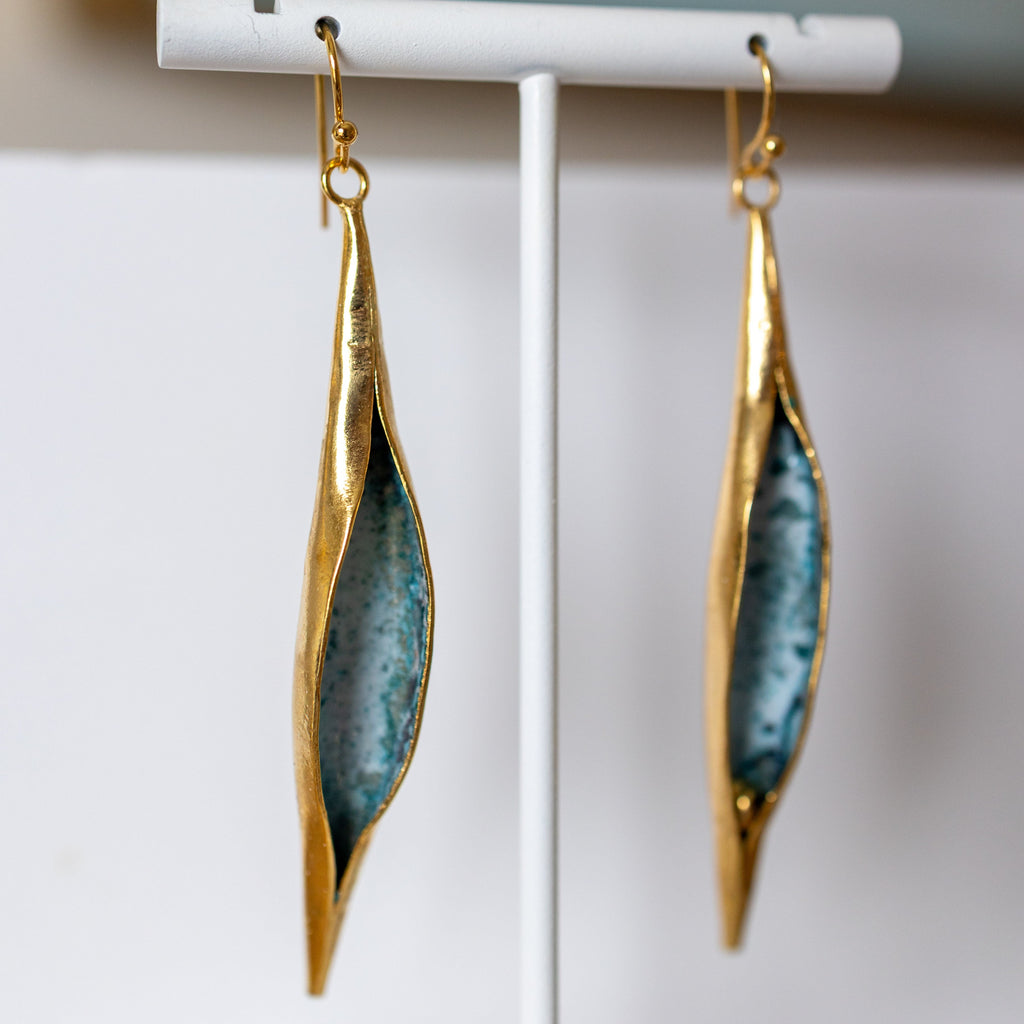 Gold and blue earrings on a white stand with a blurred background