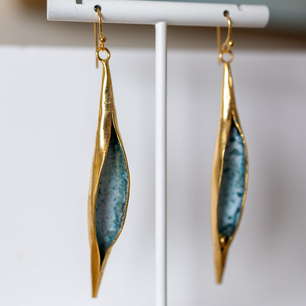Gold and blue earrings on a white stand with a blurred background