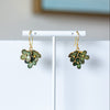 Green floral earrings on a white stand with a light blue wall in the background