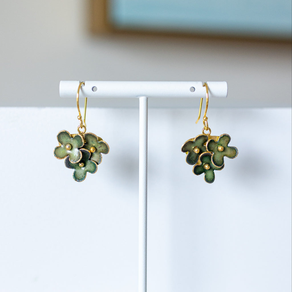 Green floral earrings on a white stand with a light blue wall in the background