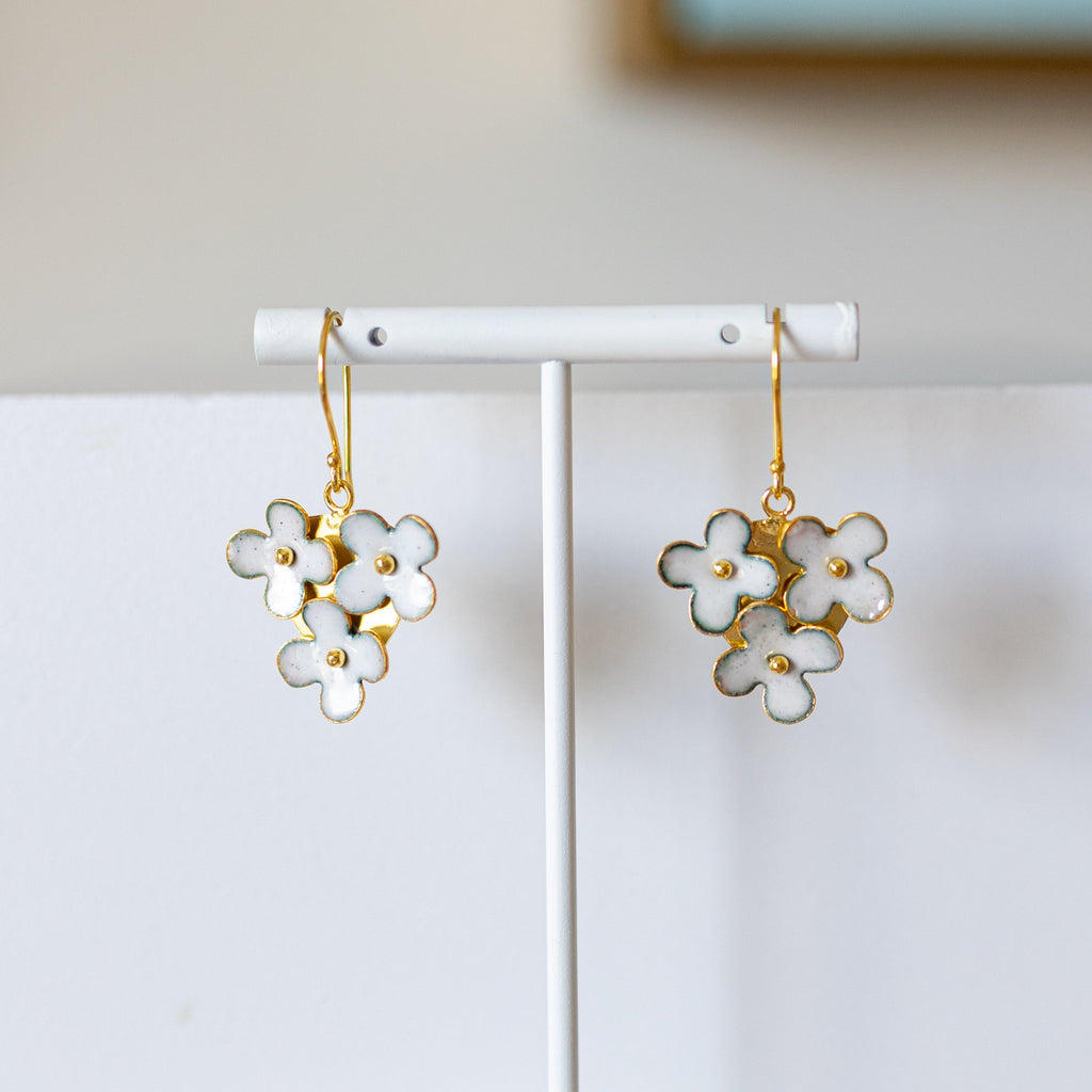 Flower-shaped earrings on a white stand against a plain background