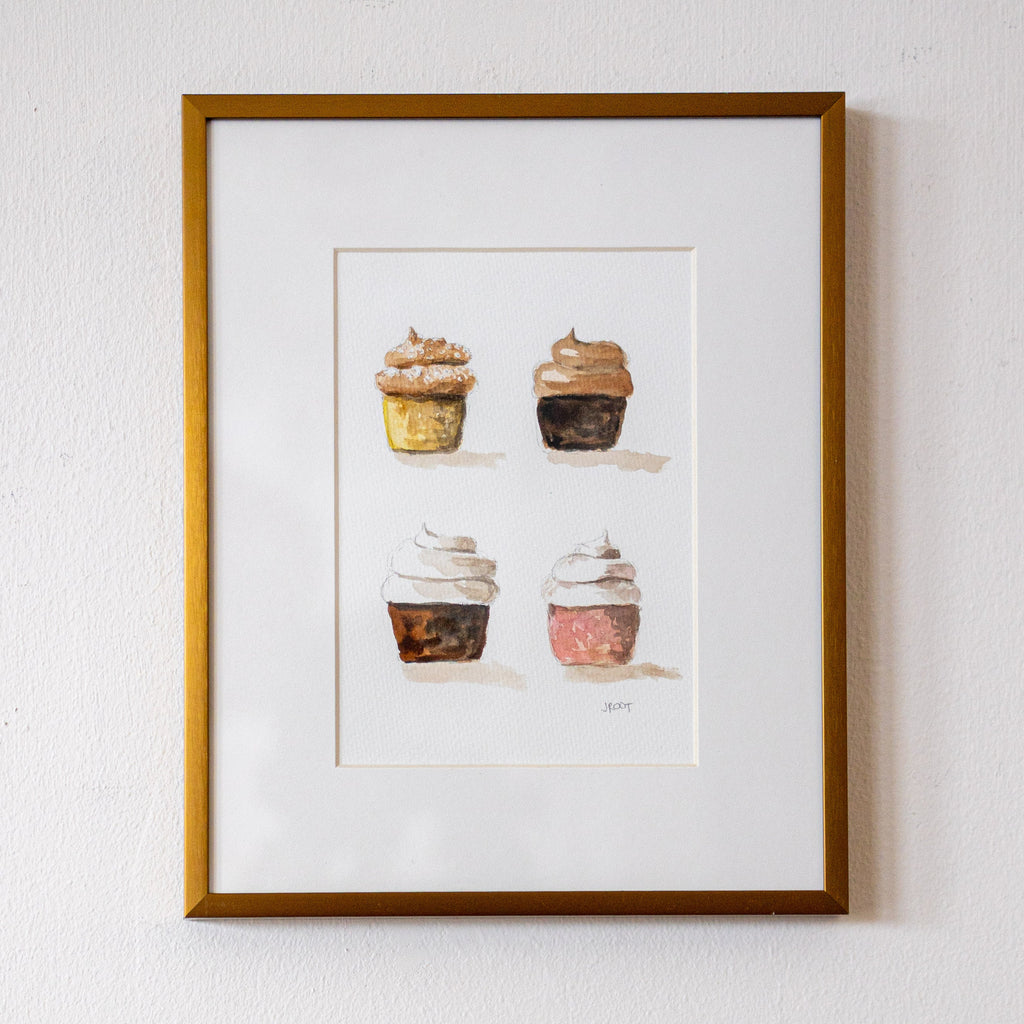 Framed artwork of four cupcakes on a white wall