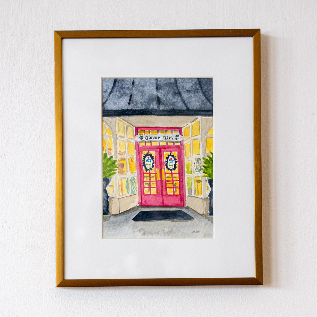 Framed artwork of a colorful building with a pink door on a white wall