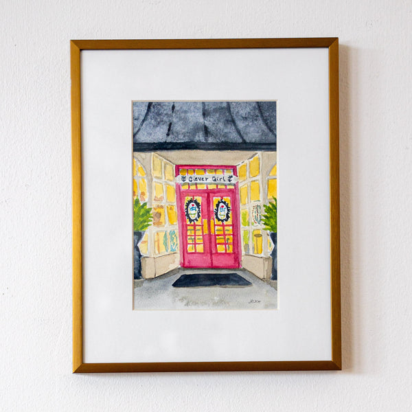 Framed artwork of a colorful building with a pink door on a white wall