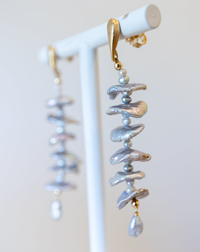 Pearl and gold earrings on a white stand with a light background