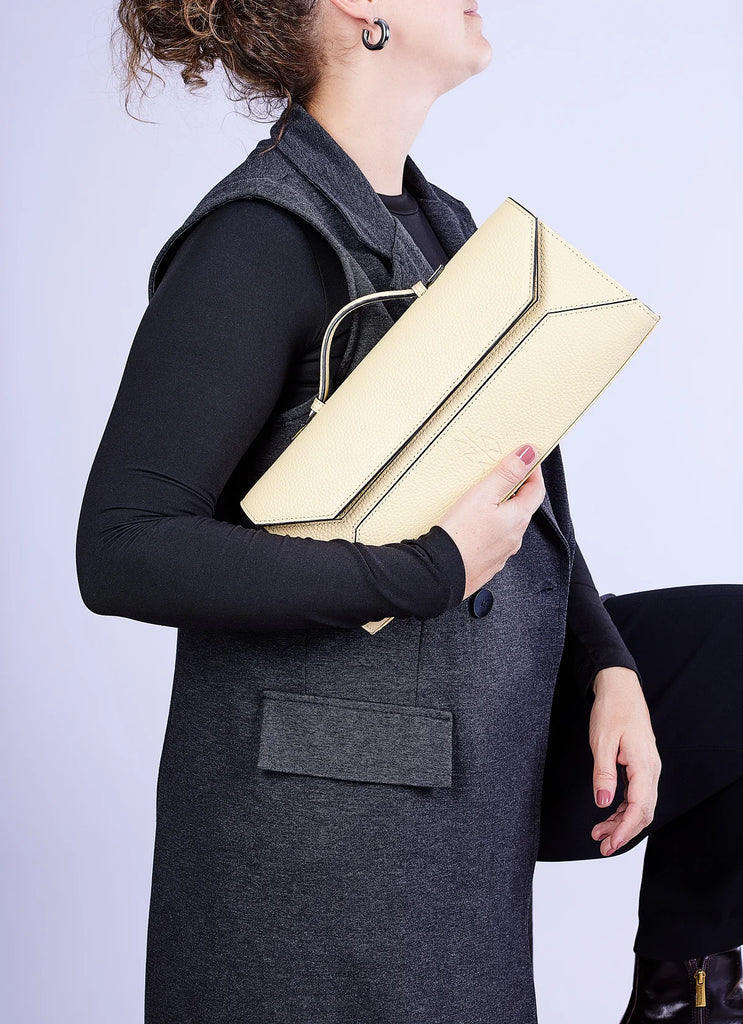 Person holding a yellow clutch bag against a light purple background