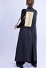 Person wearing a long dark gray dress with a beige backpack on a light purple background