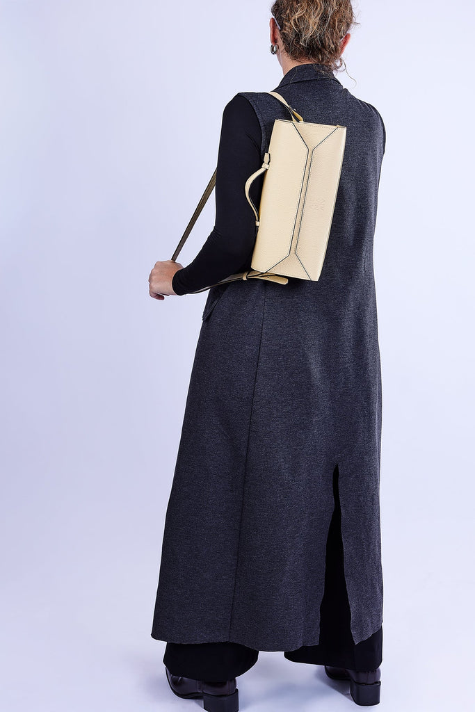 Person wearing a long dark gray dress with a beige backpack on a light purple background