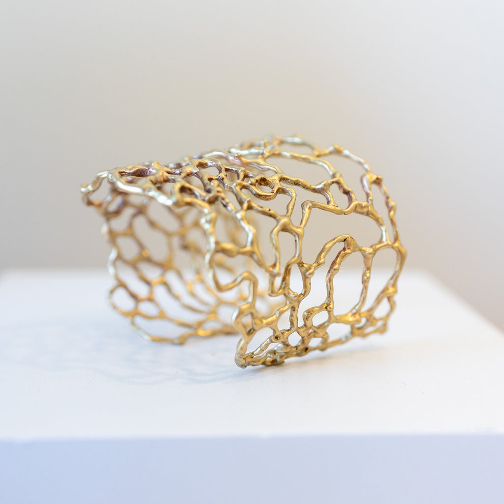 Bronze lace-style cuff bracelet on a white surface with a light gray background