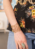 Close-up of a person wearing a bronze bracelet and floral top with a blurred background