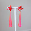 Pair of earrings with red star-shaped tops and pink teardrop-shaped bottoms on a gray background.