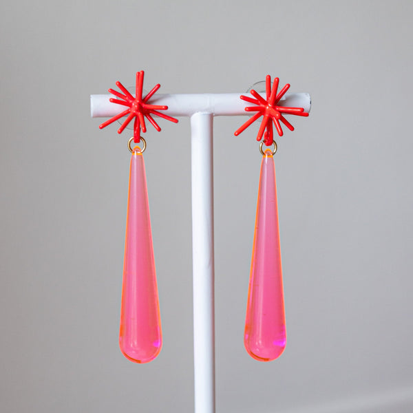 Pair of earrings with red star-shaped tops and pink teardrop-shaped bottoms on a gray background.