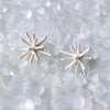 Pair of white star-shaped earrings on a textured white background