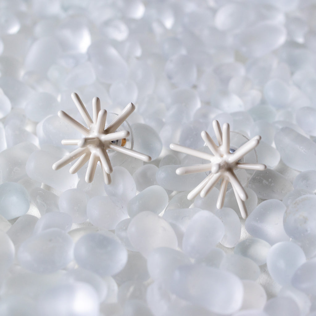 Pair of white star-shaped earrings on a textured white background