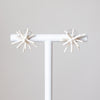 Pair of star-shaped earrings on a white stand against a light gray background