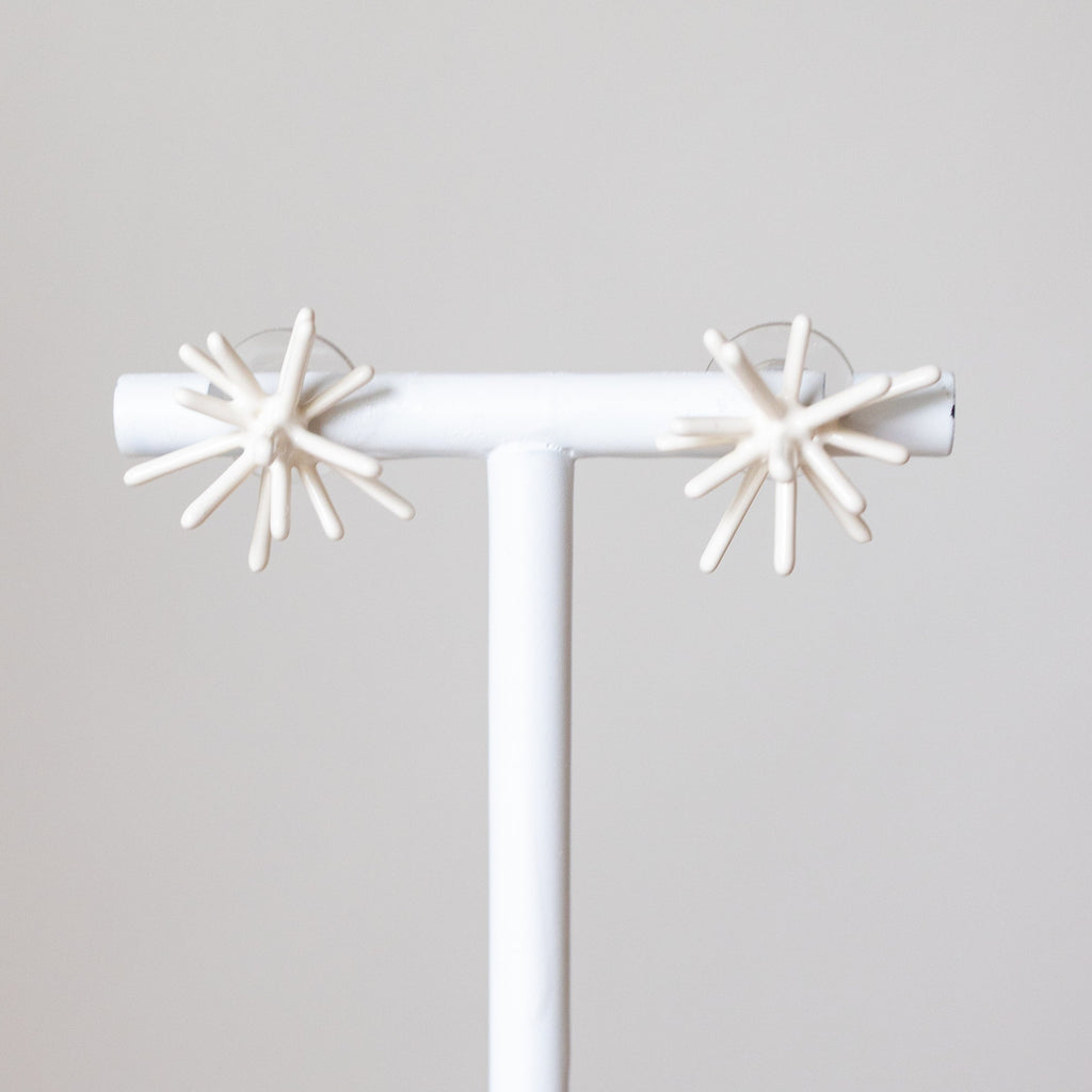Pair of star-shaped earrings on a white stand against a light gray background