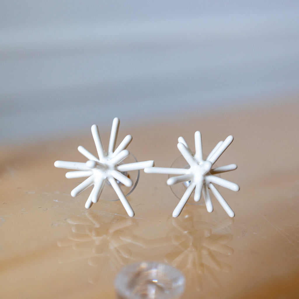 White star-shaped earrings on a reflective surface with a blurred background
