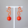 Coral earrings with spherical designs on a white stand against a gray background