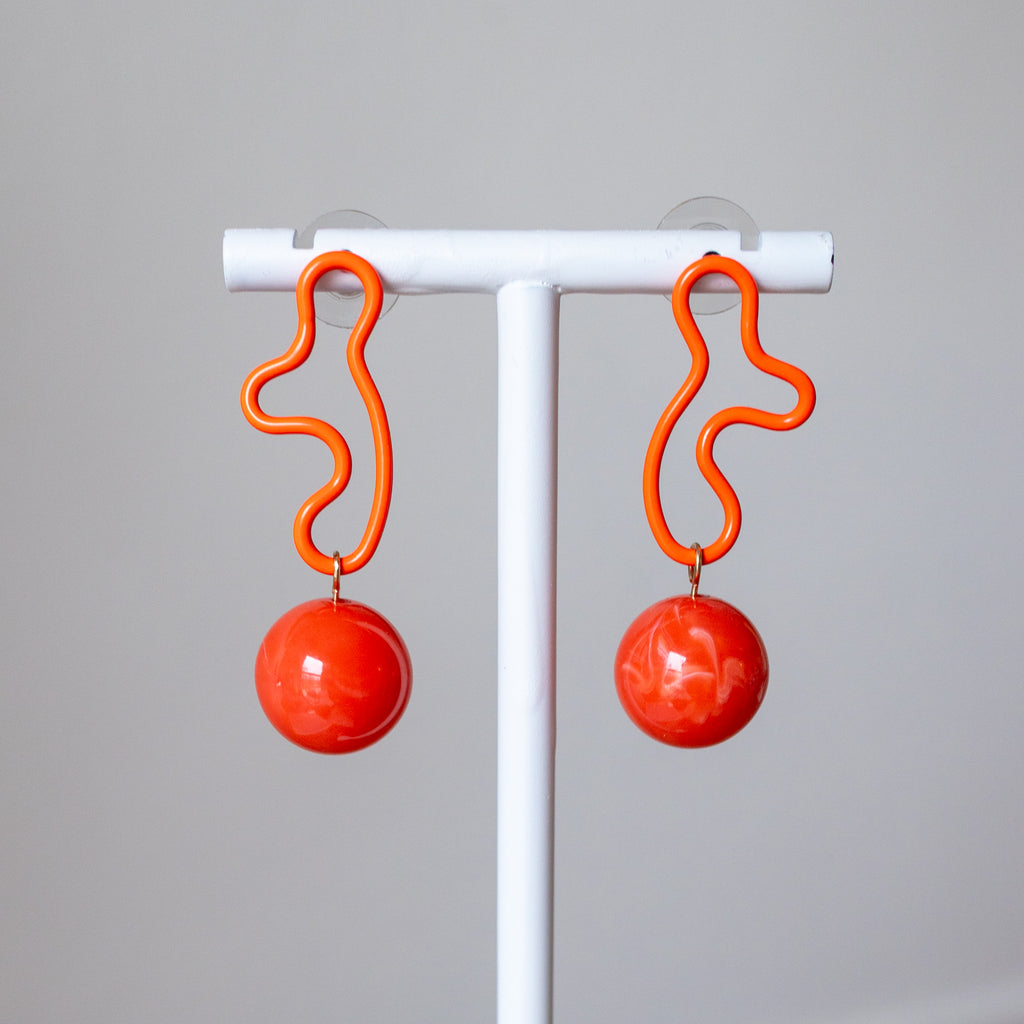 Coral earrings with spherical designs on a white stand against a gray background