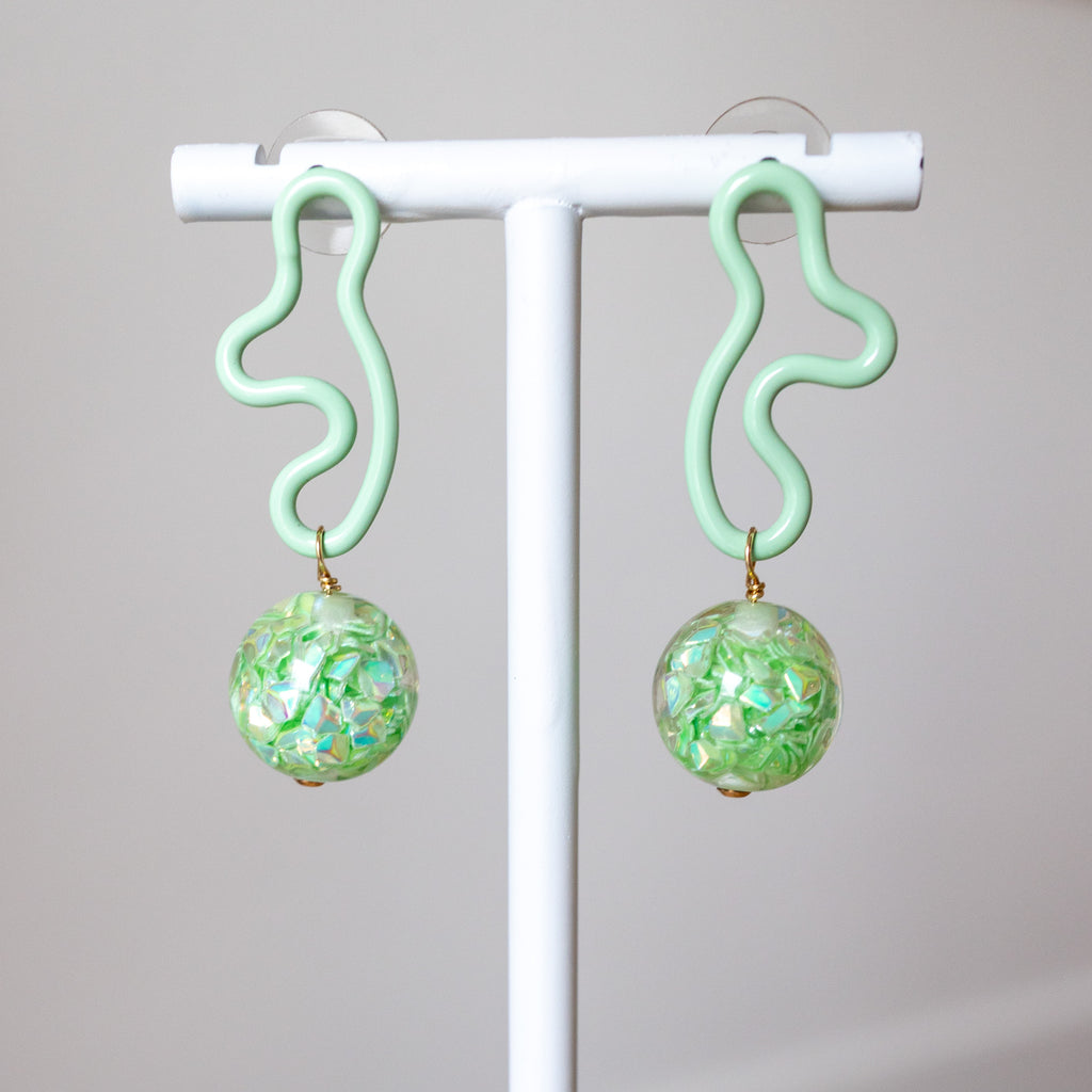 Pair of green earrings with floral patterns on a white stand against a gray background