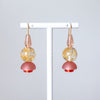 Pair of earrings with pink and gold components on a white stand against a light gray background