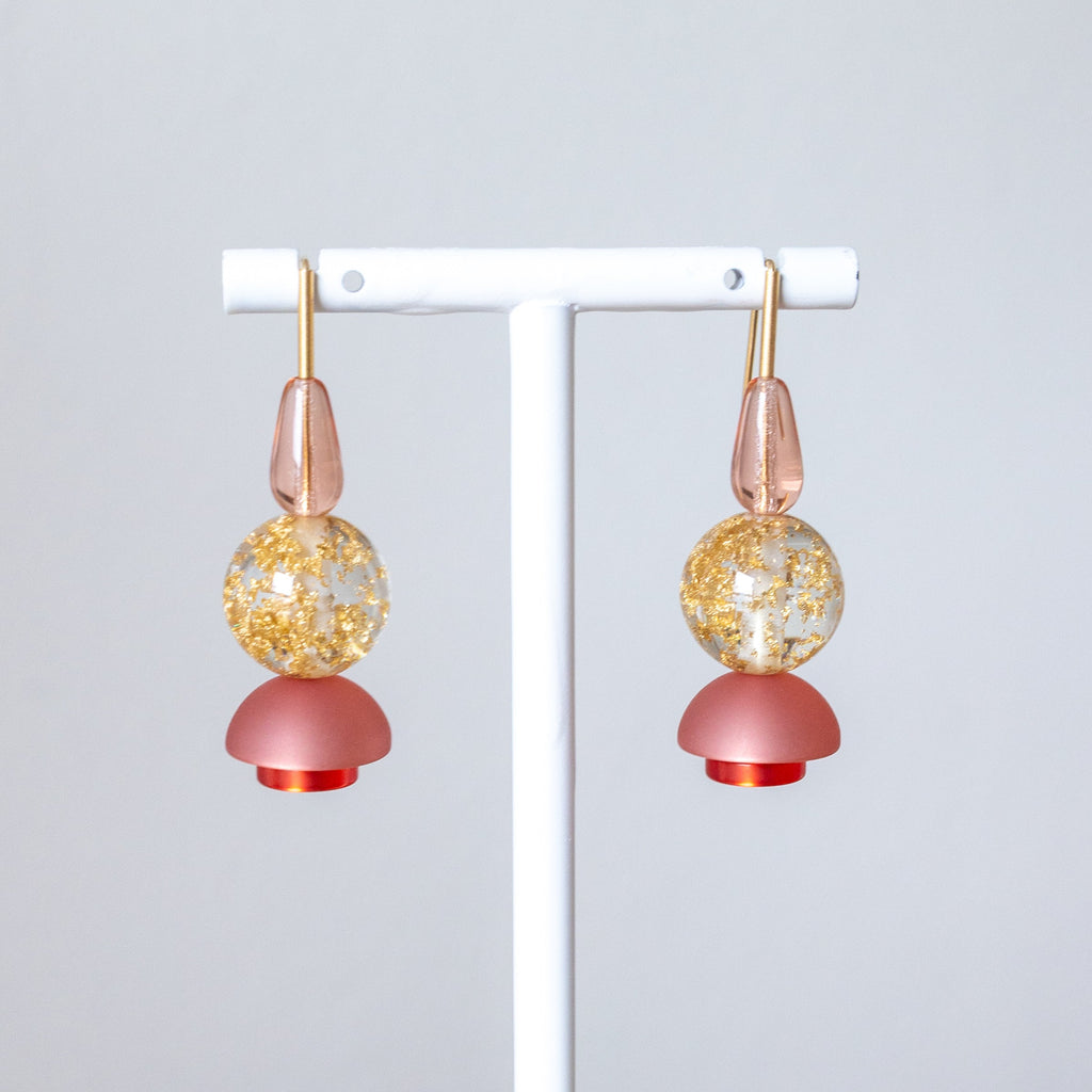 Pair of earrings with pink and gold components on a white stand against a light gray background